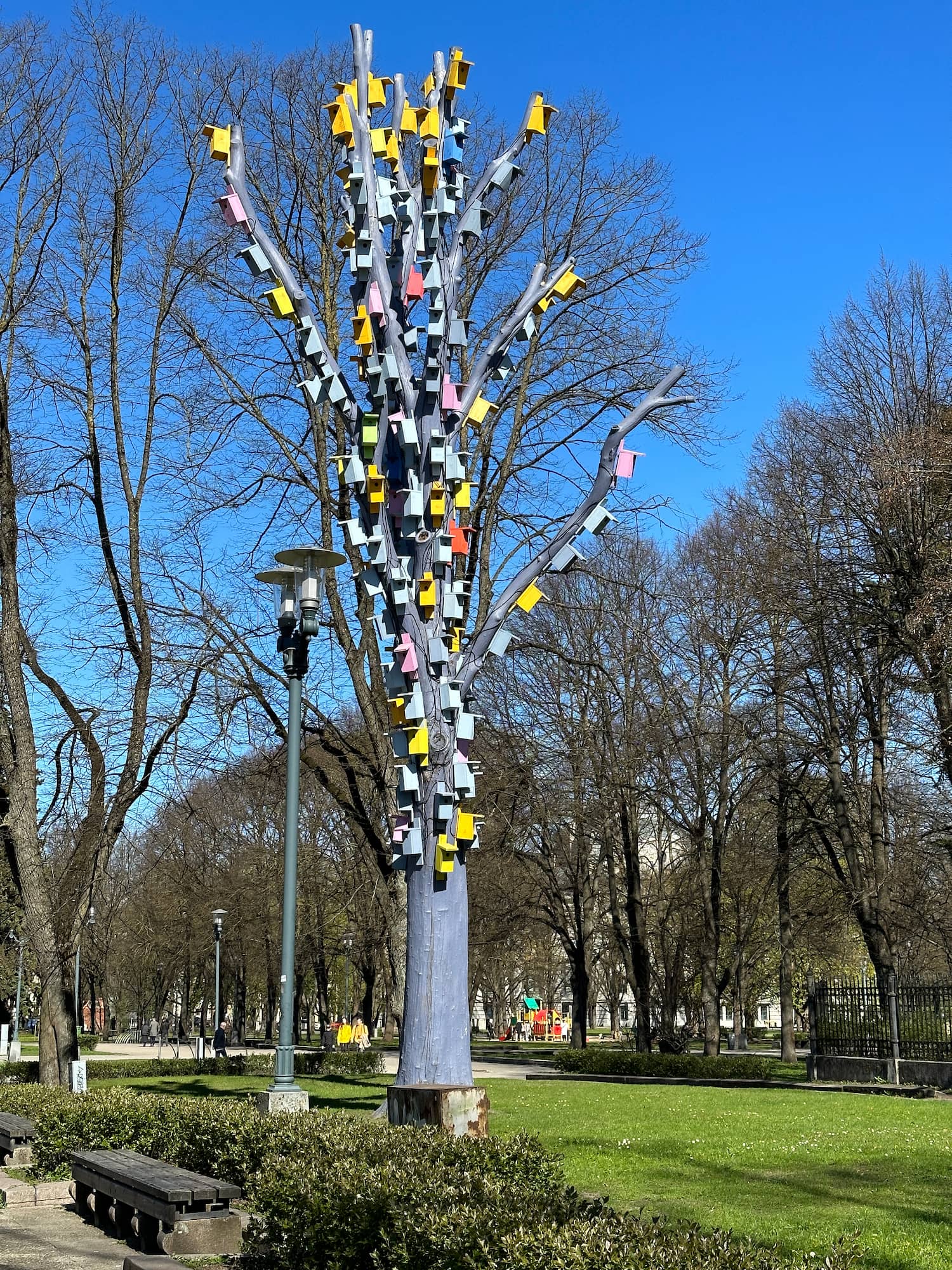 A tree painted blue with about fifty very colourful birdhouses attached to its branches